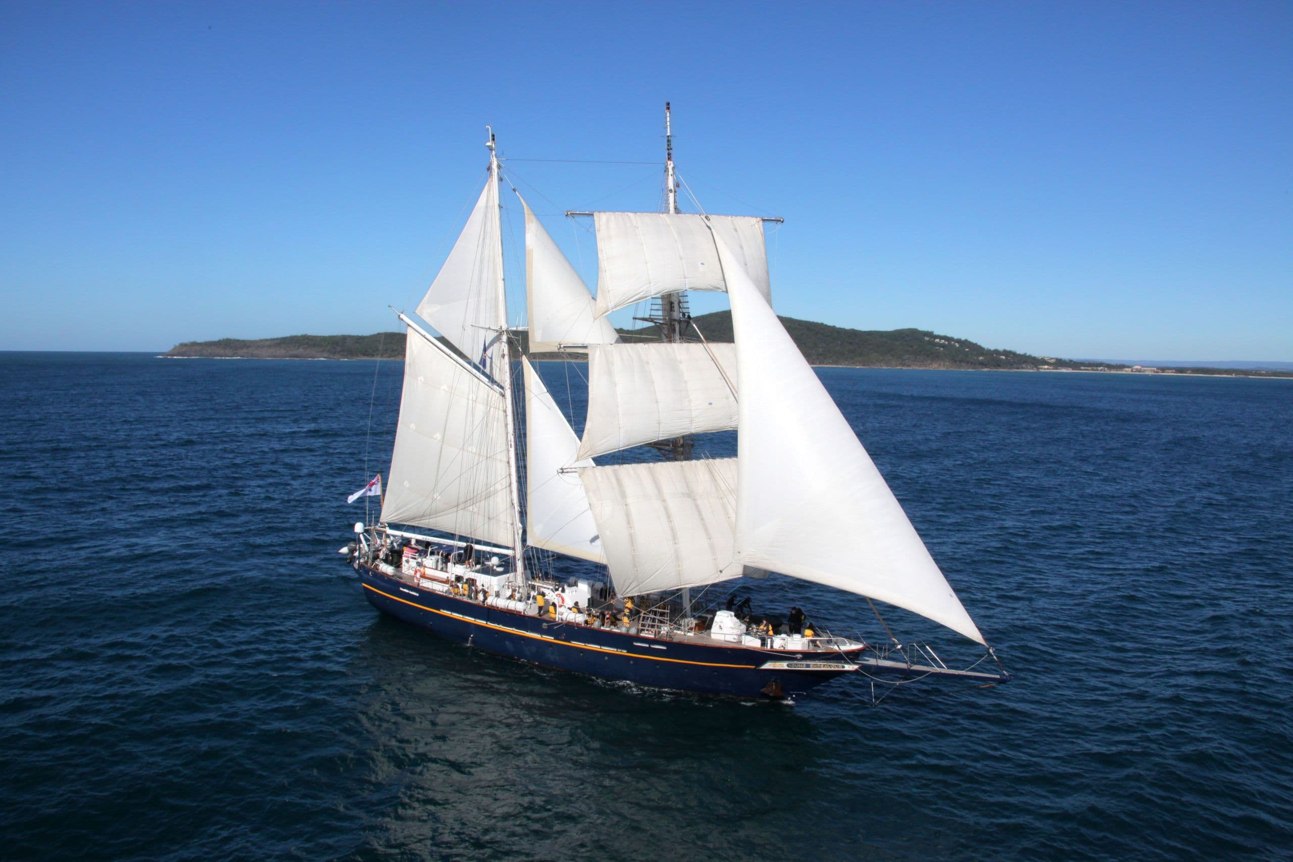 Stille zee met een eiland op de achtergrond en de Young Endeavour varend in de voorgrond