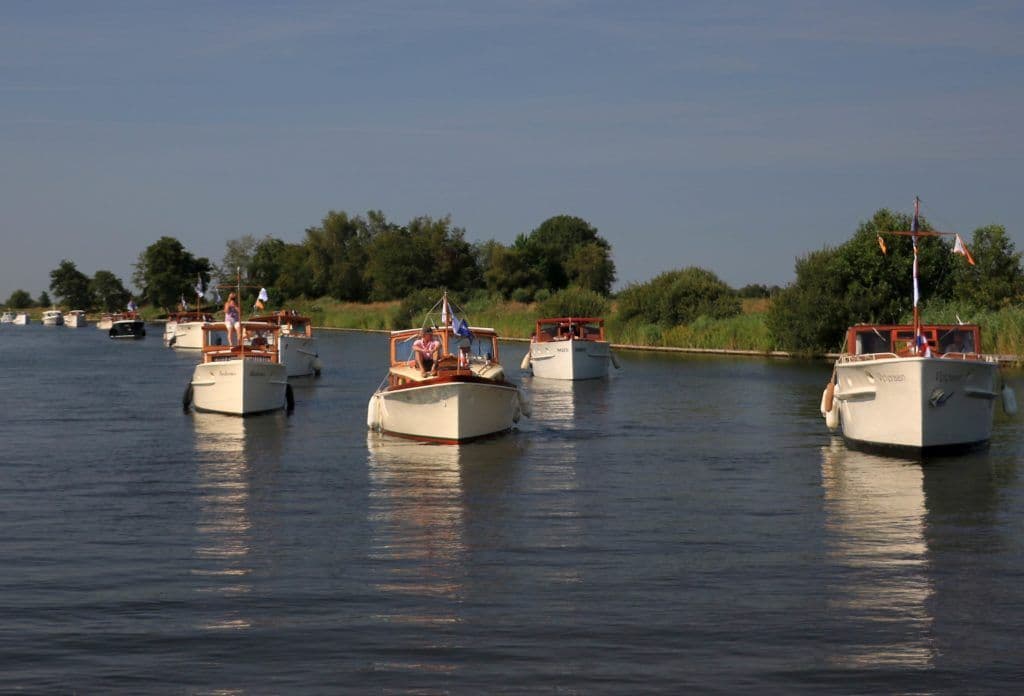 Allemaal dezelfde witte motorboten in het kanaal met gras op de oever - Vereniging Oude Glorie