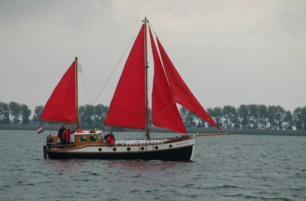 Zeilboot met rode zeilen op een rivier - Stichting Kotterzeilen en kotterbehoud