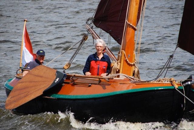 Twee mensen varen door de golven in een oude houten boot - - Vereniging Botterbehoud