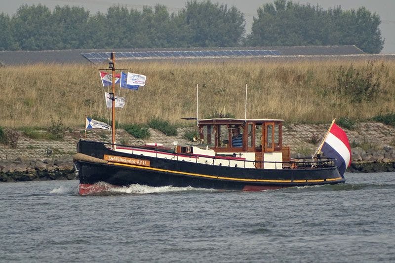 De whilhelmina met Nederlandse vlag vaart langs de oever